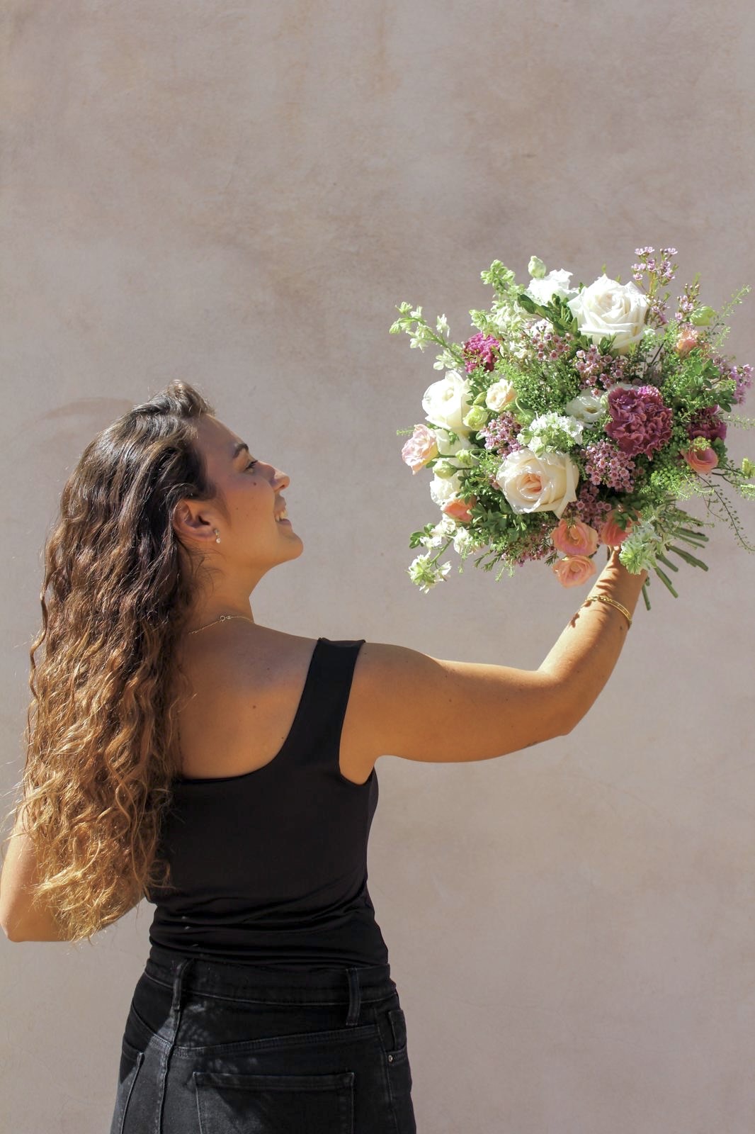 Mujer sosteniendo un ramo de flores variadas con un fondo claro.