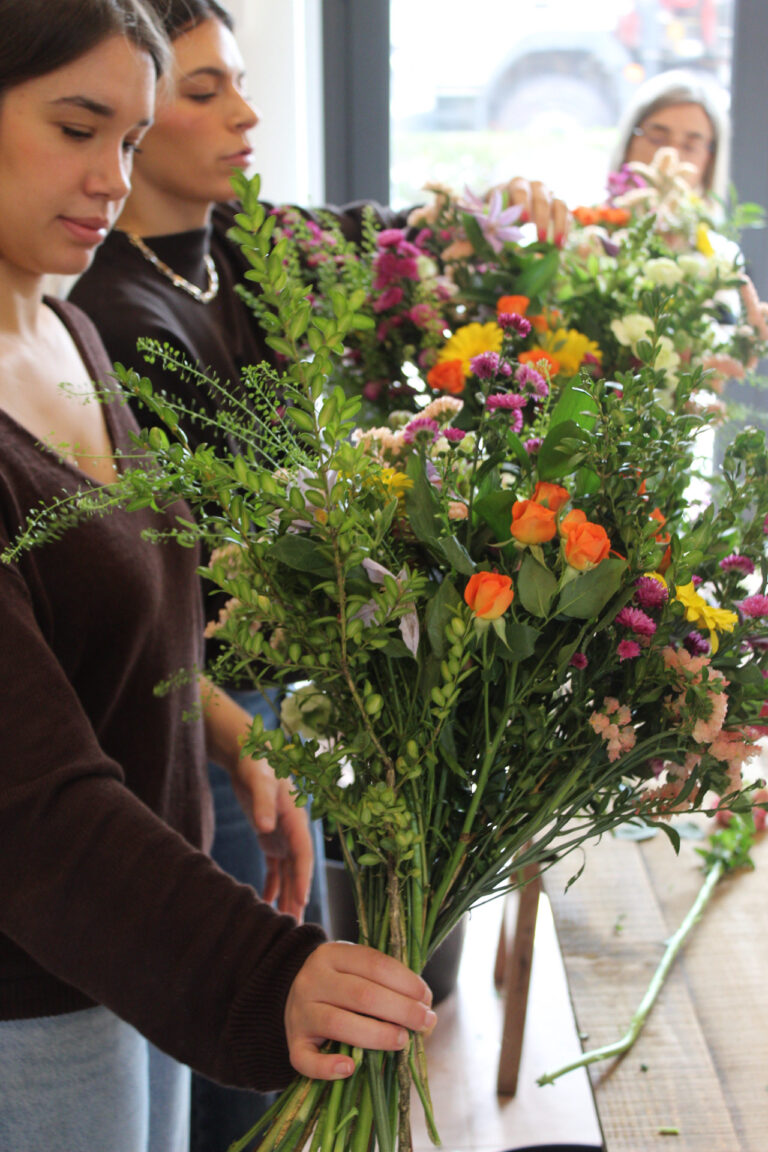 Participantes en un taller de arreglos florales, sosteniendo y organizando ramos llenos de color.