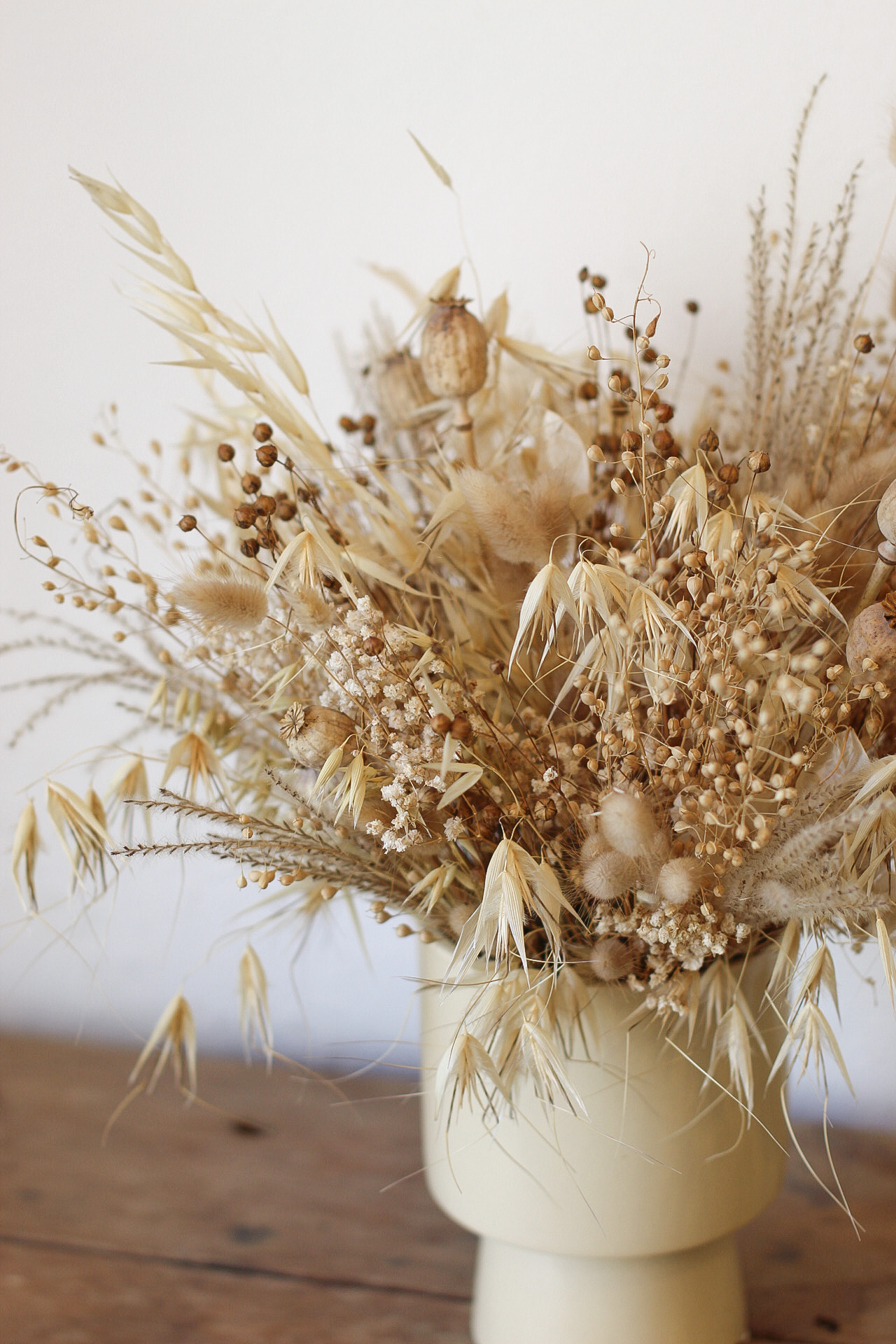 Jarrón de cerámica con arreglo de flores secas naturales en tonos beige sobre mesa de madera