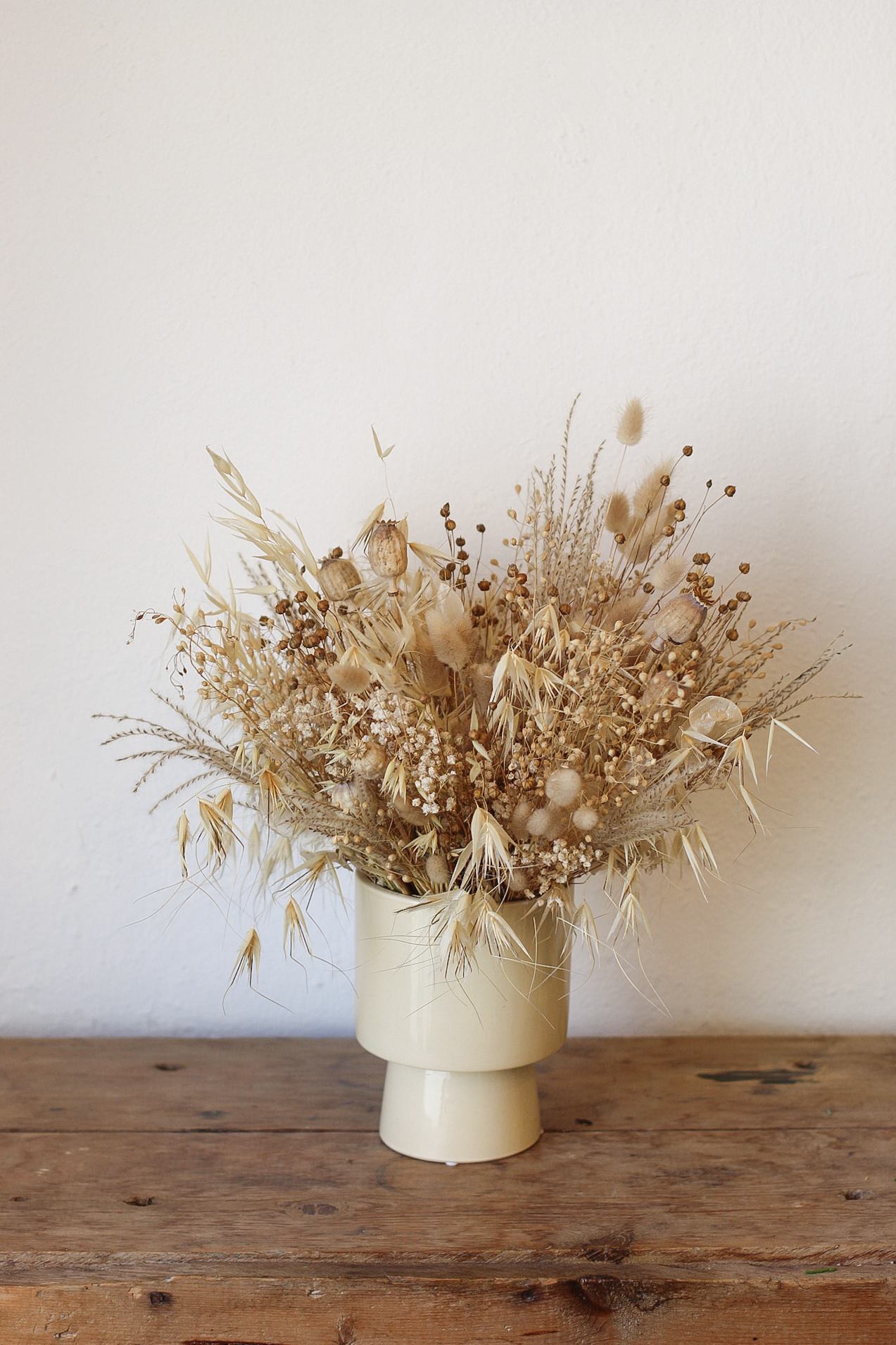 Jarrón de cerámica con arreglo de flores secas naturales en tonos beige sobre mesa de madera