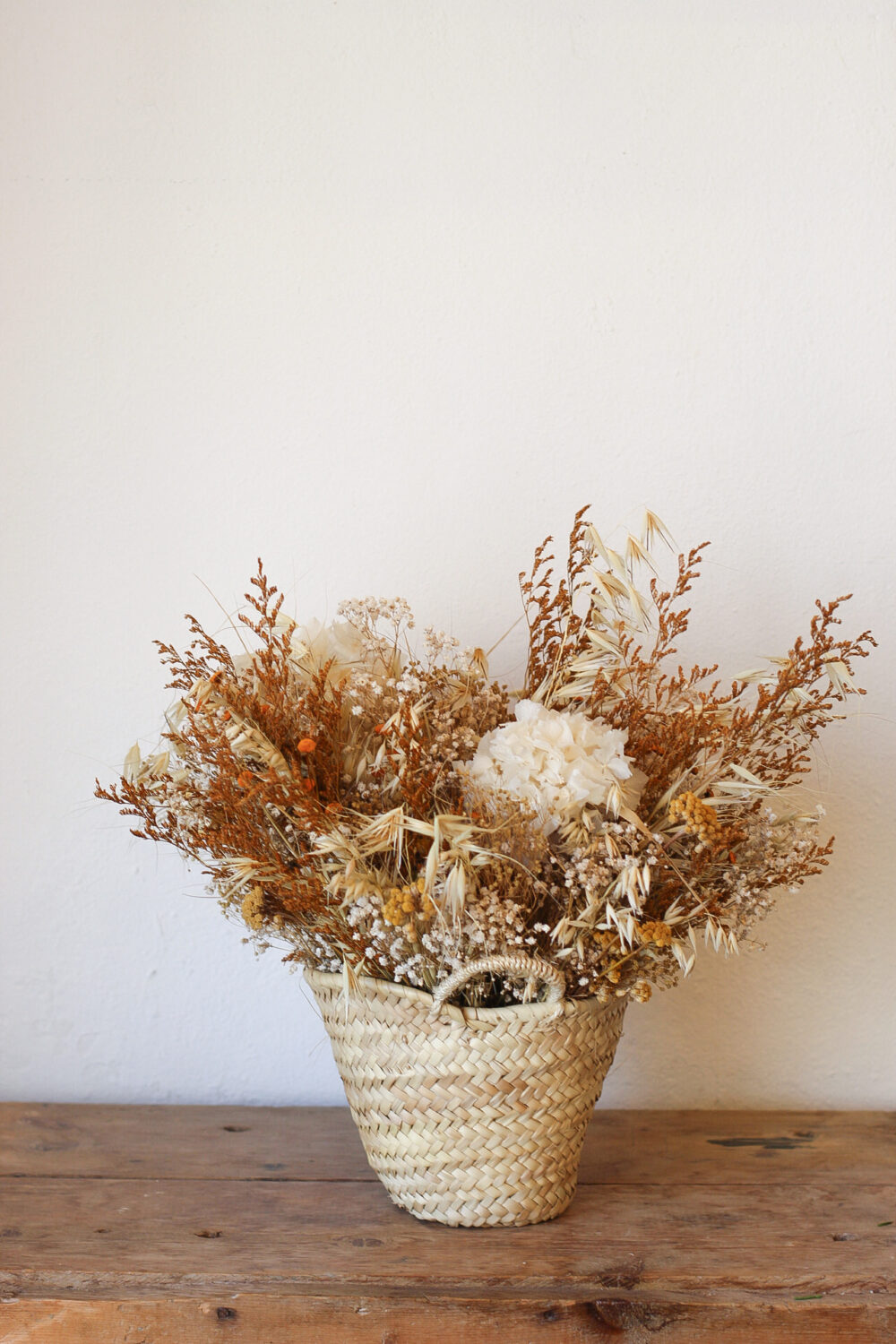 Cesta de flores secas naturales en tonos neutros sobre mesa de madera rústica