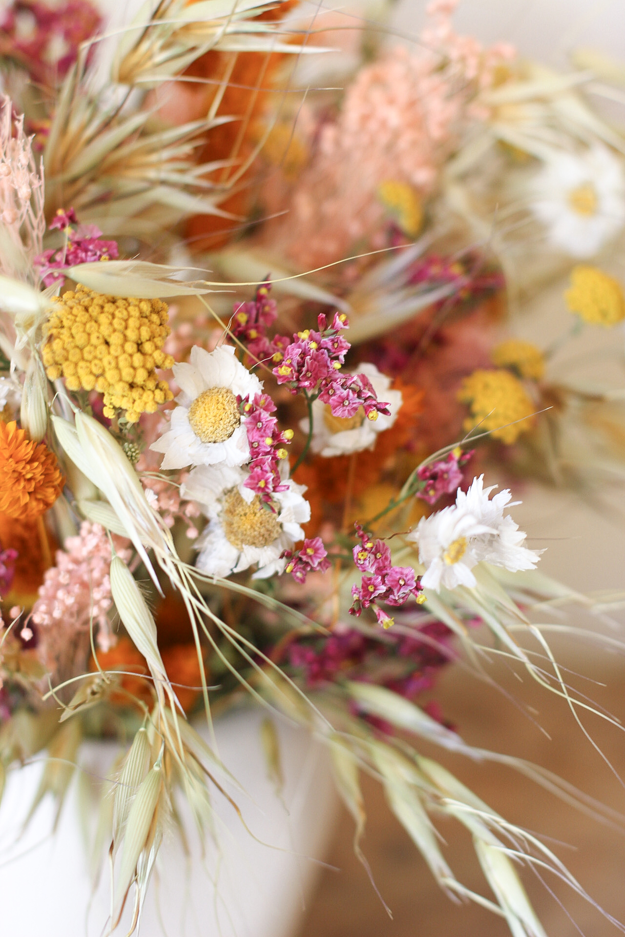 Arreglo de flores secas en tonos cálidos en jarrón blanco sobre mesa de madera rústica